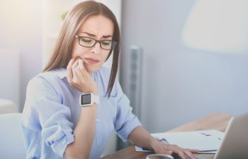 Woman suffering from dental pain due to sensitive teeth after having drunk hot coffee while working at the office.