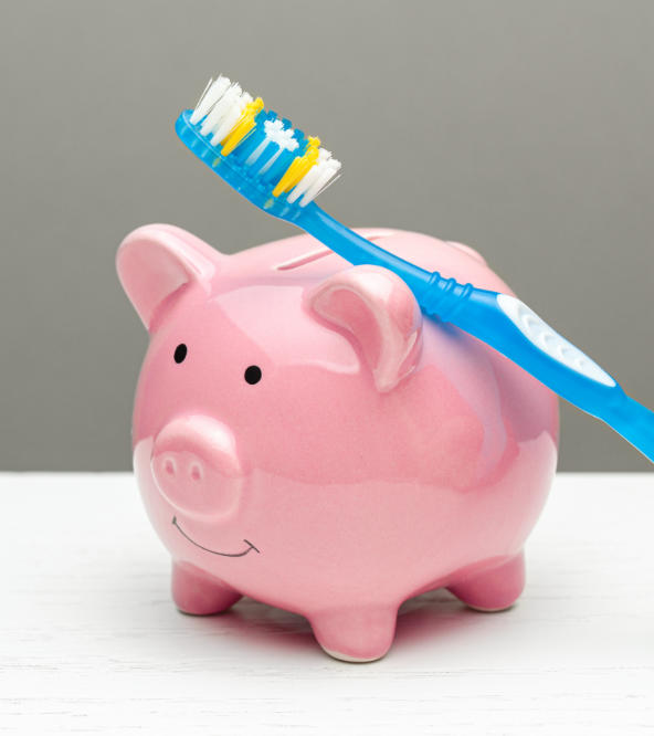 A toothbrush leaning on a piggy money-bank.