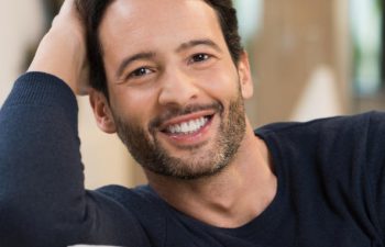 Cheerful man sitting on a sofa showing healthy teeth in his smile.