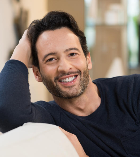 Cheerful man sitting on a sofa showing healthy teeth in his smile.