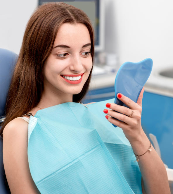 Young woman in a dental chair after treatment watching her nice teeth in a mirror.