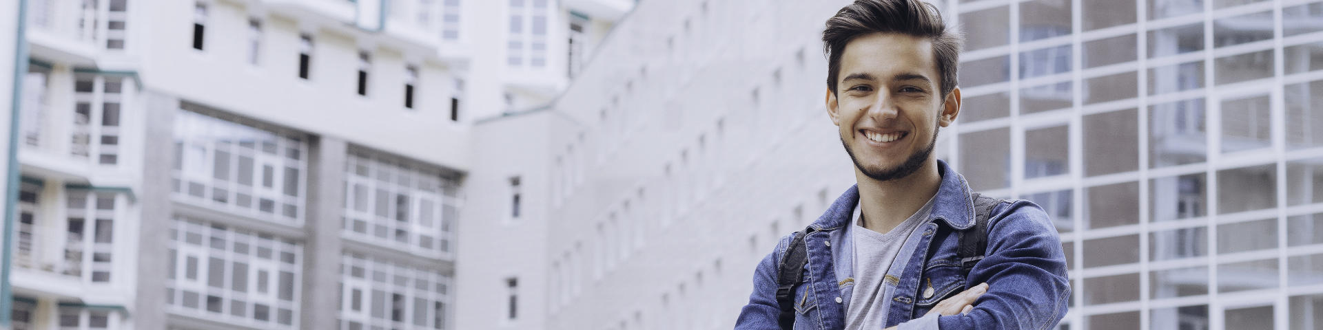 Joyful young man showing nice teeth in his smile standing in front of an office building.