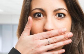 Young confused woman covering her mouth due to bad breath.