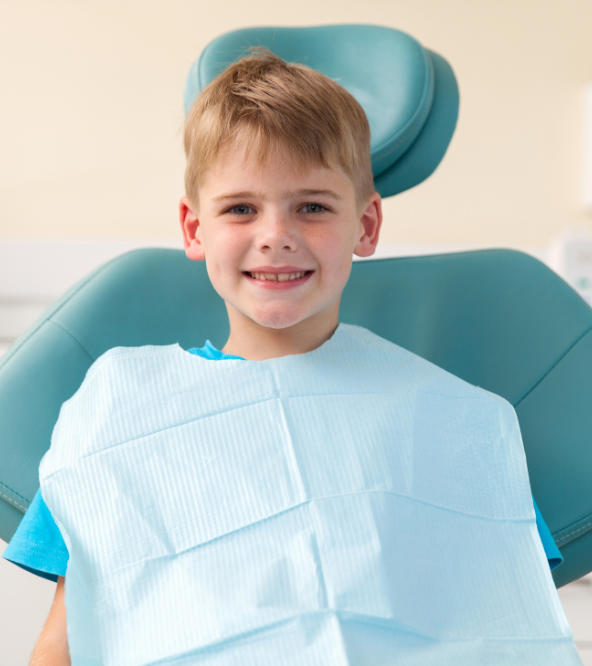 Smiling boy in a dental chair after pediatric dental treatment.