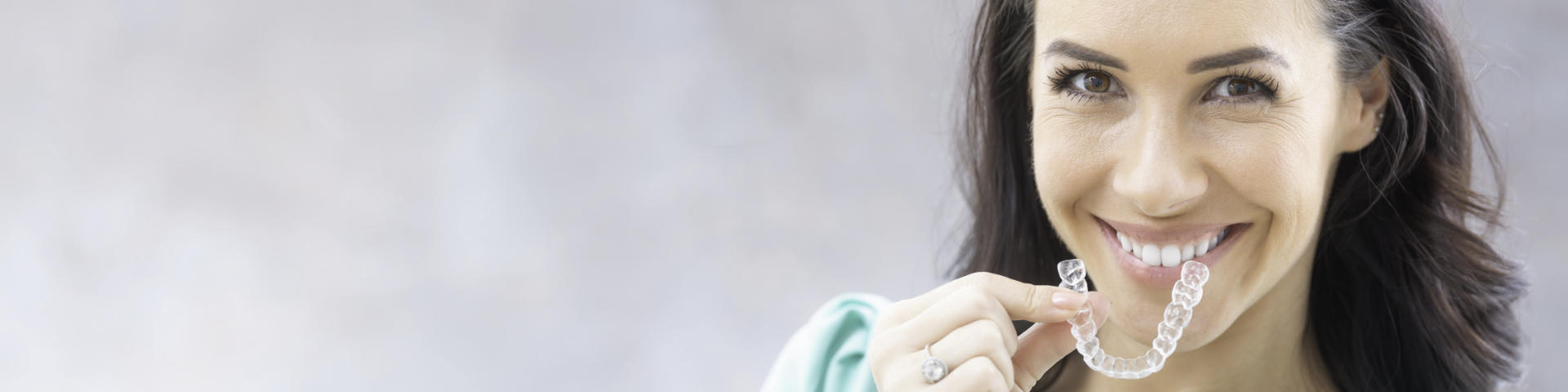 Smiling woman with clear orthodontic aligner in her hand.