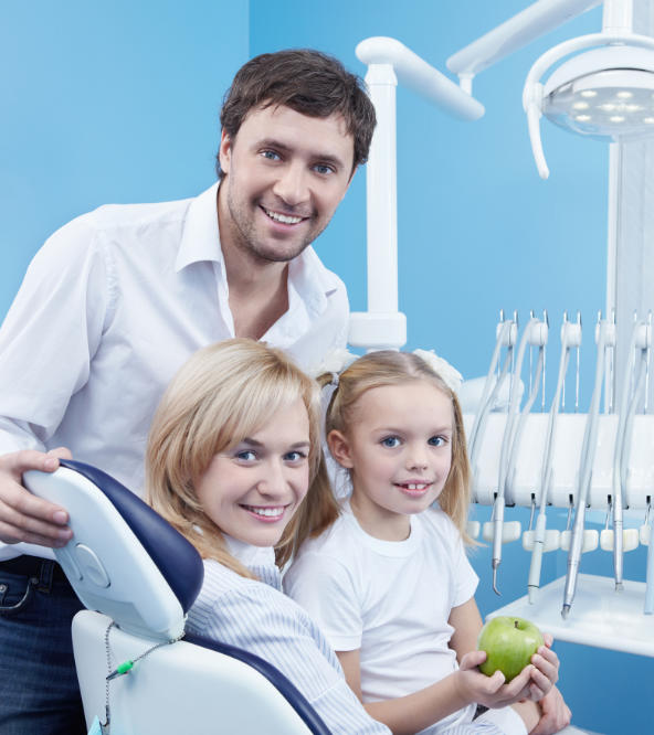 A girl holding a green apple with her parents at dentistry office.