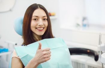 A smiling girl holdin a dental model with traditional braces in one hand and a clear aligner in the other.