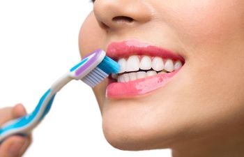 A smiling girl holdin a dental model with traditional braces in one hand and a clear aligner in the other.