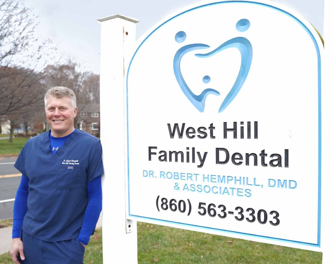 Dr. Robert Hemphill standing besides his practice sign reading West Hill Family Dental. Dr. Robert Hemphill, DMD & Associates. (860) 563-3303