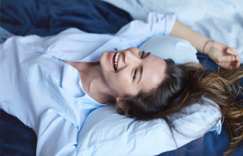 woman in blue pajamas laughs while lying on the bed