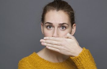 negative feelings concept - portrait of surprised beautiful 20s girl covering her mouth for bad breath or taboo,studio shot on gray background