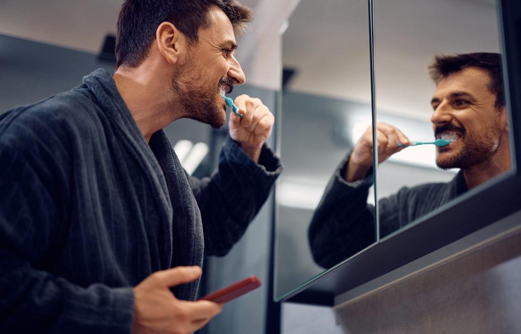 Happy man brushing his teeth while looking himself in am mirror.
